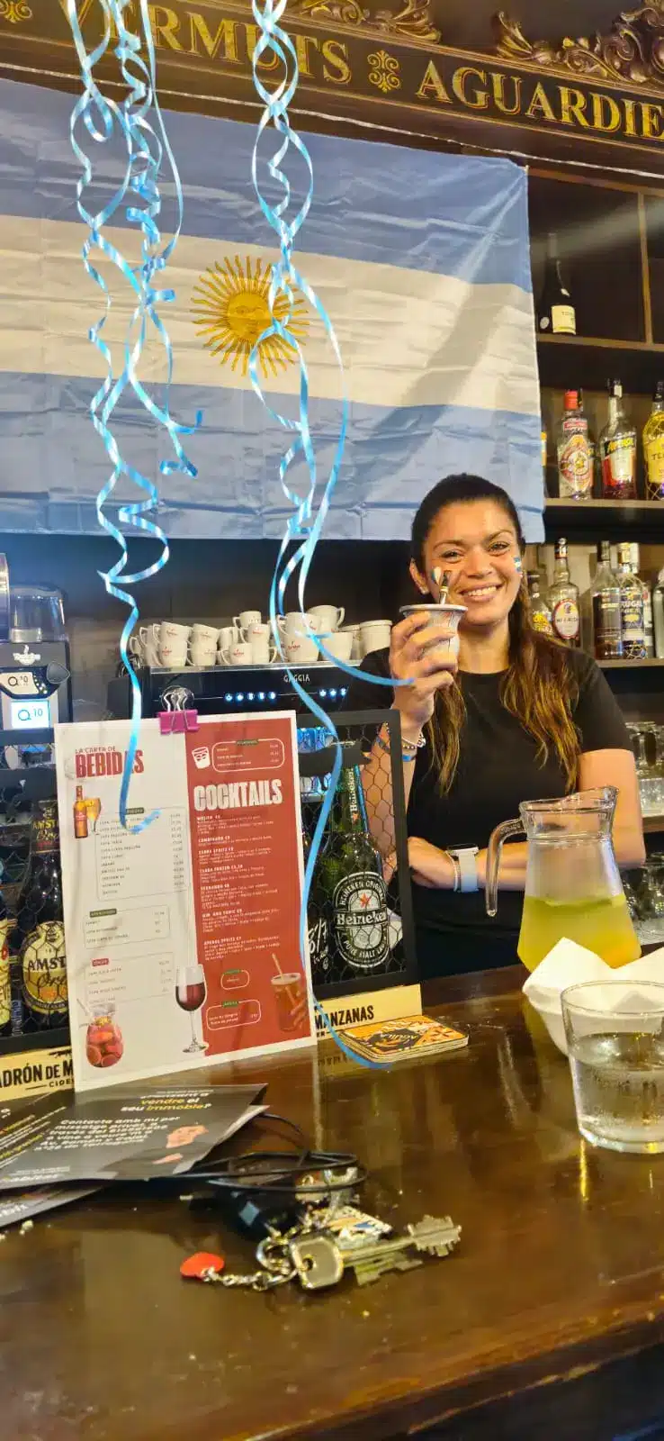 Clienta sonriendo mientras disfruta de una bebida en la barra de Buenas Raíces.
